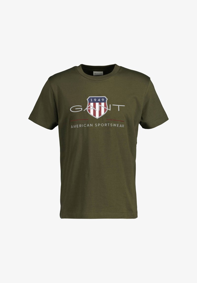 T-shirt de algodão verde oliva com um logo em forma de escudo, com listras vermelhas e azuis, e o texto "GANT AMERICAN SPORTSWEAR" em branco.