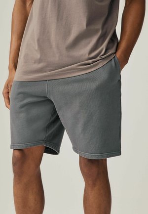 Pantaloni corti grigi realizzati in tessuto morbido, dotati di tasche laterali e una vestibilità comoda. La vita è elastica con dettagli di cucitura lungo l'orlo.