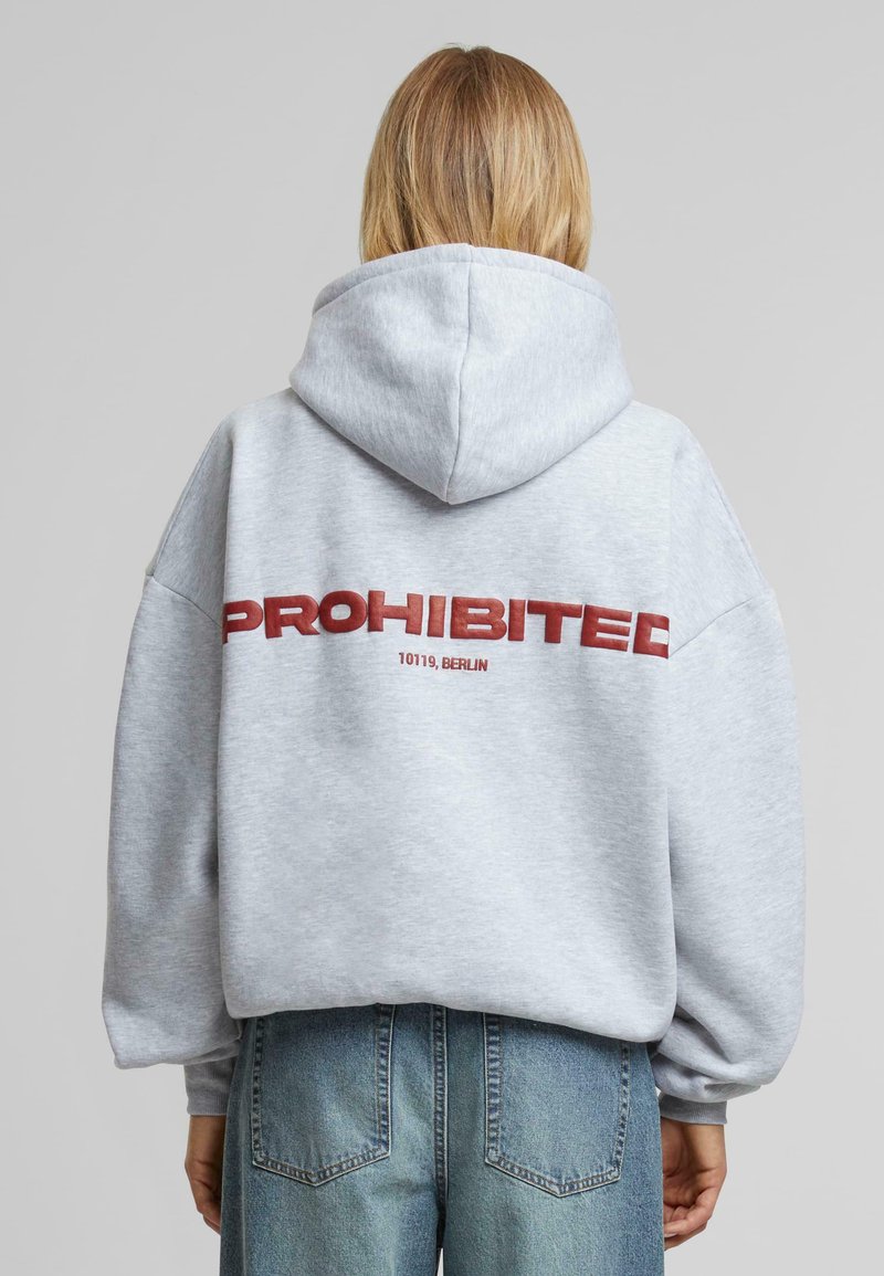 Felpa grigia con una grande scritta rossa "PROIBITO" e "10119, BERLINO" sottostante. Presenta un cappuccio ampio e una vestibilità morbida.