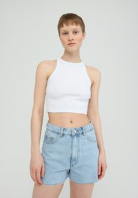 Weißes geripptes Crop-Top mit Halterneck, kombiniert mit hellblauen Denim-Shorts mit ausgefransten Kanten und vorderen Taschen.