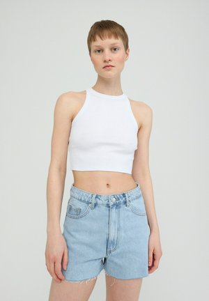 Weißes geripptes Crop-Top mit Halterneck, kombiniert mit hellblauen Denim-Shorts mit ausgefransten Kanten und vorderen Taschen.