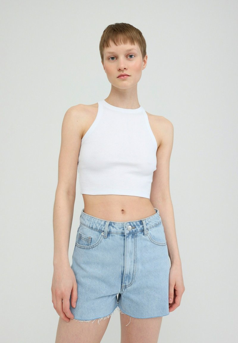 Witte geribde crop top met een halternek, gecombineerd met lichtblauwe denimshorts met rafelige randen en voorzakken.