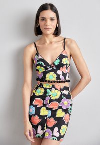 Čierny crop top s farebnými kvetinovými a pierkovými vzormi, s tenkými ramienkami a pom-pom lemovaním. V kombinácii s mini sukňou s rovnakým vzorom.