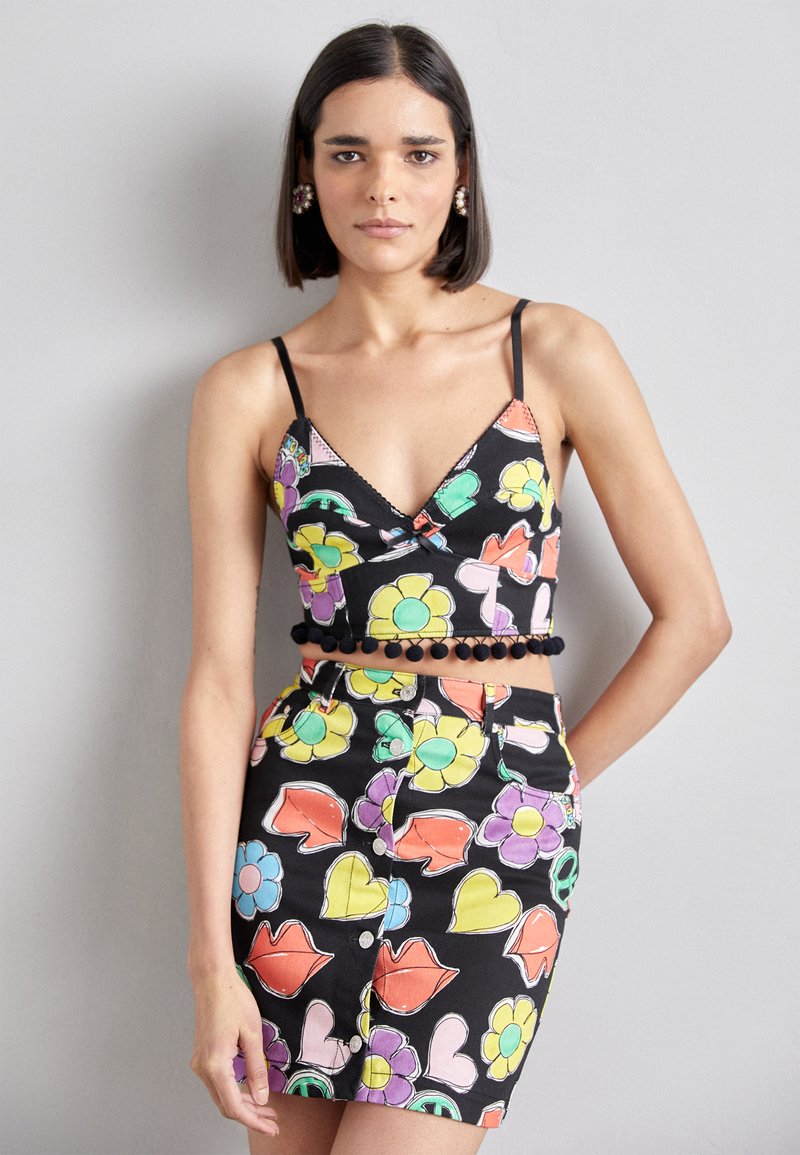 Čierny crop top s farebnými kvetinovými a pierkovými vzormi, s tenkými ramienkami a pom-pom lemovaním. V kombinácii s mini sukňou s rovnakým vzorom.