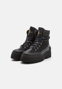 Botas negras de plataforma altas con suelas gruesas, cuellos acolchados, ojales dorados, cordones negros y el logo de "Tommy Hilfiger" en la lengüeta.
