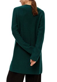 Cardigan lungo di colore verde scuro, realizzato in tessuto a coste, con taglio dritto e maniche lunghe. Senza chiusure visibili sul retro.