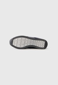 La suola della scarpa presenta una base in gomma grigia texture con un bordo nero a strisce, che mostra un motivo a griglia per la trazione.