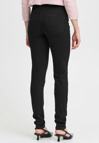 Zwarte skinny jeans met een gladde textuur, hoge taille en standaard achterzakken. Geverfd met zwarte open-taille hakken.
