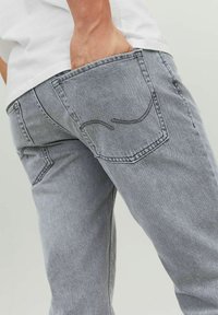 Jean en denim gris avec une coupe droite. Doté d'une poche arrière avec des coutures contrastées et une texture légèrement délavée.