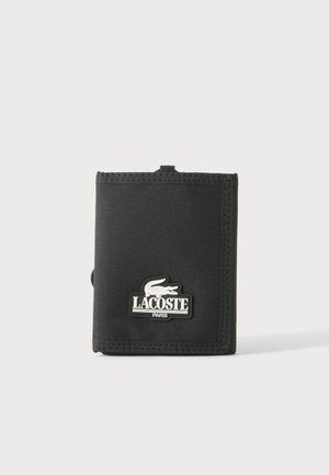 Zwarte stoffen drieluiksportemonnee met gestikte randen en wit Lacoste Paris-logo met een krokodil aan de voorkant.