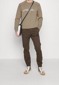 Ljusbrun sweatshirt med vit text, bruna byxor och gröna högskaftade sneakers med vita och tan-färgade detaljer. Axelremsväska i grönt och vitt.