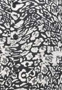 Czarno-biała tkanina w wzór zwierzęcy z wyraźnie widocznymi guzikami z przodu.