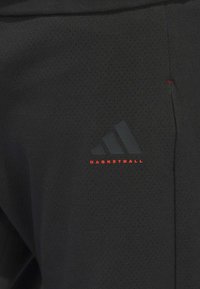 Zwarte basketbals shorts van geperforeerde stof met een adidas-logo en de tekst "BASKETBALL" in het rood. Eenvoudig ontwerp met een moderne pasvorm.