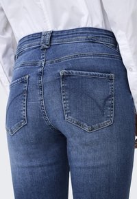 Jeans de denim azul oscuro con un diseño ajustado, que presentan dos bolsillos traseros con detalles de costura y un corte de cintura alta.