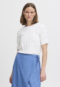 Hvid bluse med hulmønster og korte ærmer, med en rund halsudskæring; parret med en lys blå indpakningsskørter med sidetie-detail.