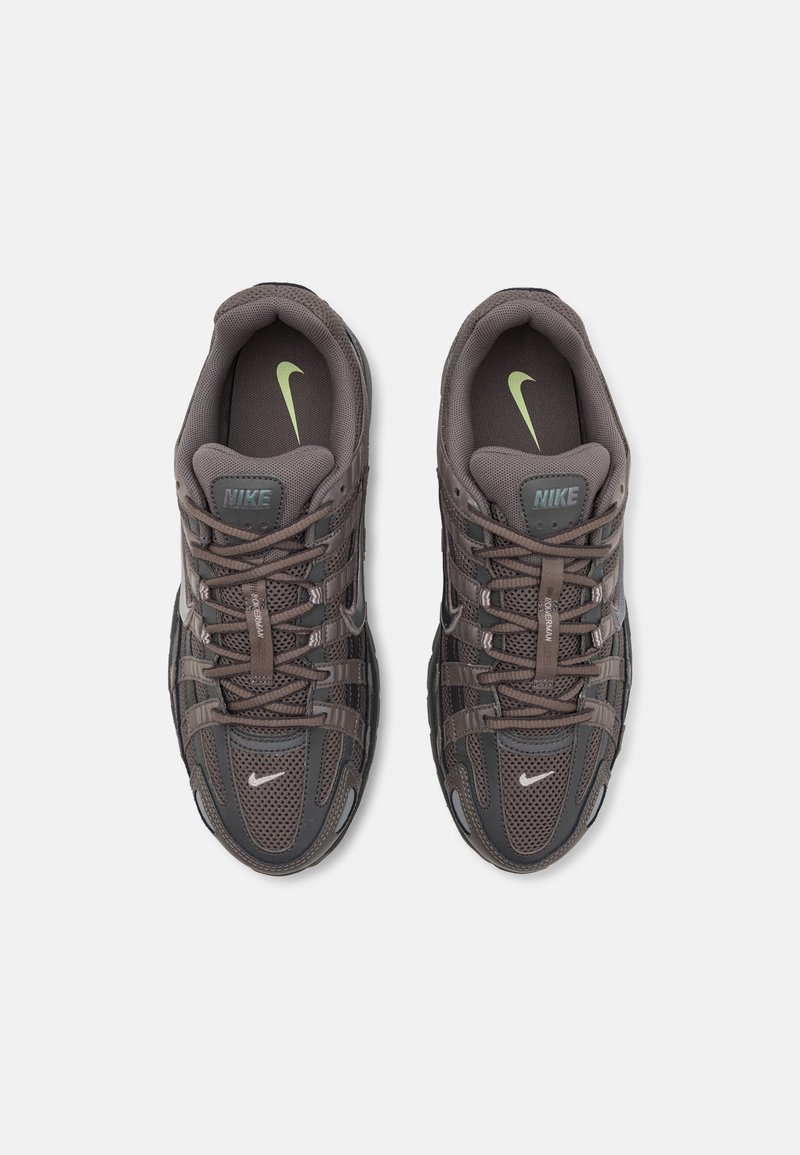 Zapatillas Nike grises con parte superior de malla, acentos reflectantes y punta redondeada. Presentan un diseño de cordones y un logotipo de Nike verde en la lengüeta.