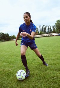 Blue athletic jersey with a patterned texture and orange accents, paired with black shorts and socks, as a player interacts with a multicolored soccer ball on grass.
