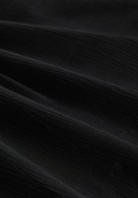 Tissu noir avec une texture fine et subtile. Le matériau semble lisse et légèrement réfléchissant, avec des plis ondulés créant de la dimension.