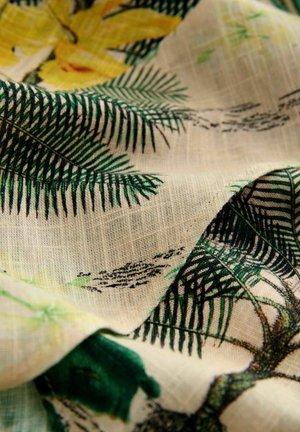 Tissu à motif floral avec des fougères vertes et des fleurs jaunes sur un fond texturé beige. Matériau léger et doux.
