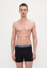 Schwarze Boxershorts mit einem blauen elastischen Bund, der das "BJÖRN BORG"-Logo trägt; figurbetontes Design, weicher Struktur und mittellange Beinform.