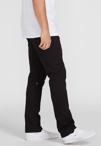 Zwarte broeken van stevige stof, met een slim-fit ontwerp, een platte voorkant en een klein logo op het onderbeen. Draag ze met witte schoenen.