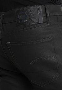 Svarta denimjeans med en strukturerad yta, kontrasterande sömmar och en läderetikett på midjebandet med logodetalj.