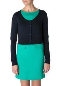 Mörkblå kort cardigan med knappar, i kombination med en turkos klänning med rund halsringning och två framfickor. Mjuk, slät textur.