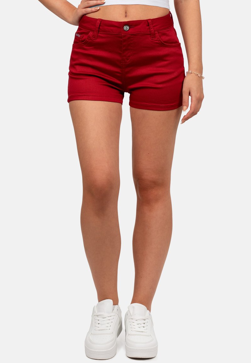 Shorts in denim rosso con design aderente, quattro tasche e chiusura con bottone. Abbinati a sneaker bianche. Tessuto liscio, lunghezza al ginocchio.