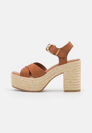 Jasnobrązowe zamszowe sandały na platformie z plecioną jucie obcasem, z krzyżującymi się paskami i paskiem na kostkę z złotą klamrą.
