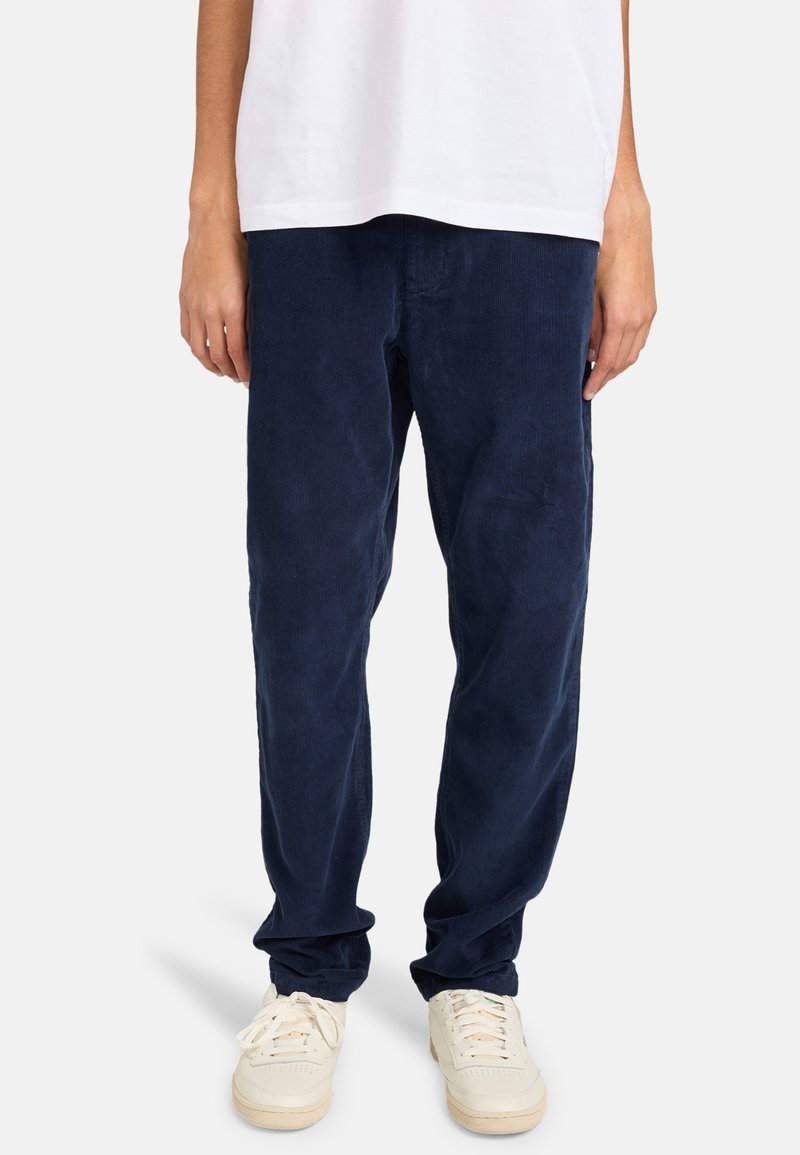 Pantalones de pana de color marino con un corte relajado, que presentan una textura en la tela y puños elásticos, combinados con zapatillas blancas.