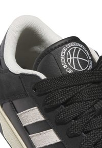 Zwart-witte basketbalsneaker met gestructureerde zwarte veters, witte strepen aan de zijkant en basketballogo op de tong.