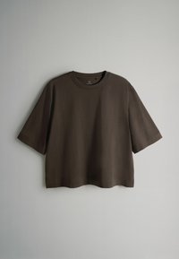 Brązowa bawełniana koszulka z krótkim rękawem, okrągłym dekoltem i luźnym krojem. Prosty dół bez widocznych wzorów czy ozdób.