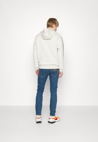 Sweatshirt cinza claro com capuz, complementado por um par de jeans azuis. Apresenta um design horizontal na manga, finalizado com ténis de várias cores.