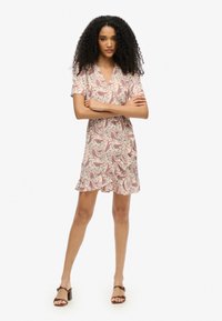 Vestido con estampado de paisley floral en tejido ligero, con escote en V, mangas cortas y un dobladillo con volantes. La paleta de colores incluye rojo y crema.