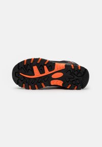 Black athletic shoe sole with deep treads, featuring orange accents and patterns for traction. Smooth texture with flexible rubber.