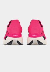 Ζευγάρι φωτεινά ροζ αθλητικά παπούτσια με λευκές και μαύρες ενισχυμένες σόλες, από πίσω σε απλό φωτεινό φόντο.
