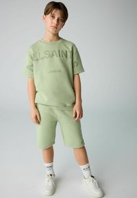 Lys grøn kortærmet sweatshirt og shorts sæt med præget "ALLSAINTS LONDON" tekst. Båret med hvide sneakers og logo-sokker.