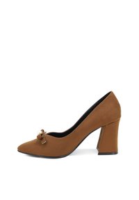 Scarpa con tacco alto in suede marrone, con punta affusolata, caratterizzata da un dettaglio a fiocco con perla e un design del tacco spesso.