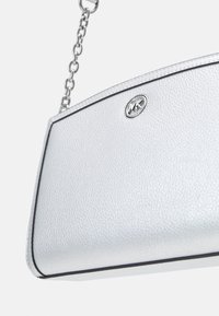 Borsa a tracolla in pelle argentata con una forma strutturata, caratterizzata da rifiniture nere, una tracolla a catena e un emblema con logo sul davanti.