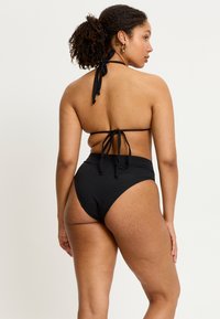 Bikini noir avec un soutien-gorge à nouer autour du cou et un bas taille haute. Tissu lisse avec une finition mate et un design minimaliste.