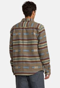 Camicia marrone a fantasia con strisce orizzontali blu, verdi e rosse, con chiusura a bottoni e vestibilità comoda. Design del tessuto strutturato.