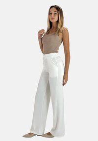 Pantalons larges blancs avec un design sur mesure ; dotés de poches avant et d'une texture lisse. Associés à un haut sans manches à côtes marron clair.