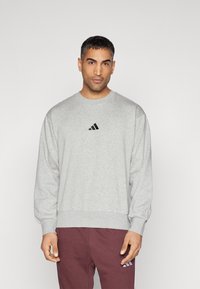 Grå sweatshirt gjord av en blandning av bomull, med rund halsringning och elastiska ärmslut. Svart Adidas-logotyp på bröstet.