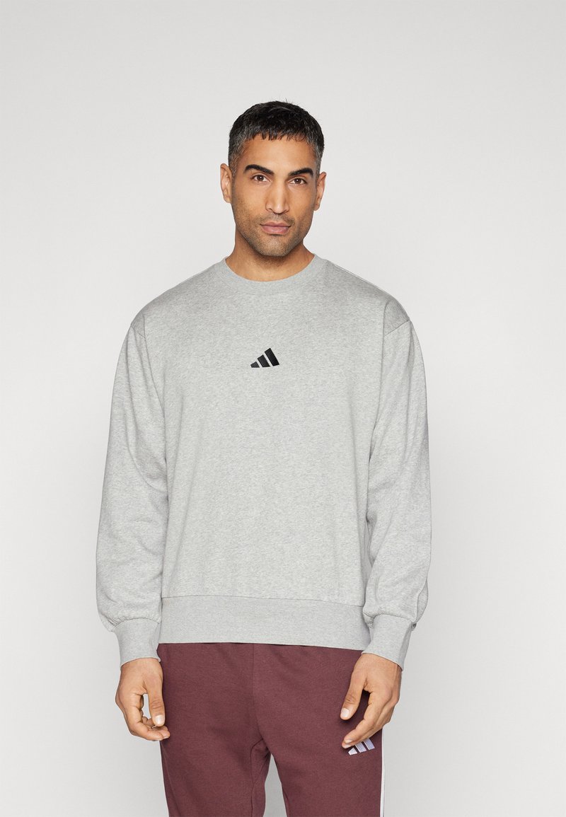 Grå sweatshirt gjord av en blandning av bomull, med rund halsringning och elastiska ärmslut. Svart Adidas-logotyp på bröstet.