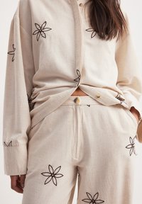 Beige katoenen shirt en broekset met zwarte geborduurde bloempatronen, knoopsluitingen en een comfortabele pasvorm met lange mouwen.