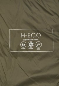 Olivgrüner Stoff mit der Aufschrift "H-ECO NACHHALTIGER STOFF" in Weiß, versehen mit Symbolen für Nachhaltigkeit, Umweltfreundlichkeit und Wasserabweisung.