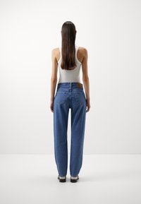 Lys grå tanktop i kombinasjon med blå, løstsittende jeans med klassisk femlommersdesign og et brunt lærmerke på livet.