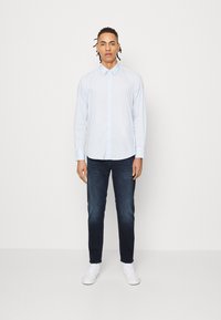 Hellblaues Hemd mit klassischem Kragen, kombiniert mit dunklen Jeans und weißen Sneakers. Das Hemd hat lange Ärmel und ist leicht tailliert.