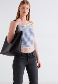 Crop top rayé bleu et blanc avec des bordures jaunes, associé à un jeans gris foncé. Le mannequin tient un grand sac fourre-tout noir mat.
