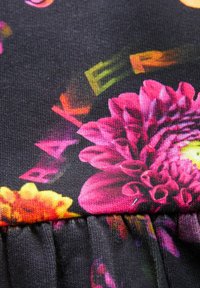 Lilleline kangas, kus on erksad roosa ja kollase värviga õied mustal taustal, märgatava tekstuuri ja kokku kogutud äärega detailiga.